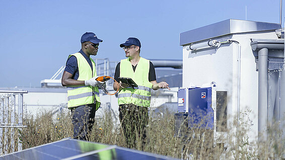 [Translate to Deutsch (AT):] Two Leadec employees on factory roof with photovoltaic panels.